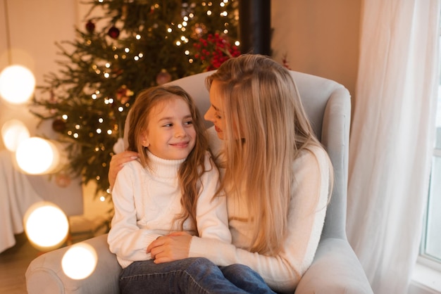 Mutter und Kind, Mädchen, Tochter, die Weihnachtsferien feiern, sitzen im Stuhl über dem Weihnachtsbaum im Zimmer Wintergrußzeit Feier der Mutterschaft