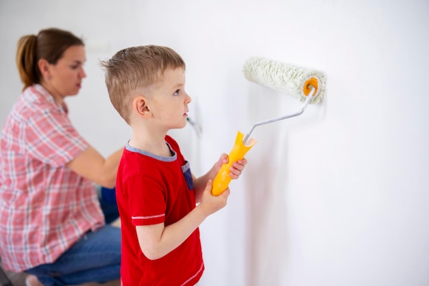 Mutter und Kind malen die Wand mit Farbe mit Rolle und Pinsel