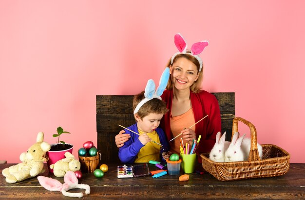 Mutter und Kind malen Ostereier. Nettes Kind, das am Ostertag Hasenohren trägt.