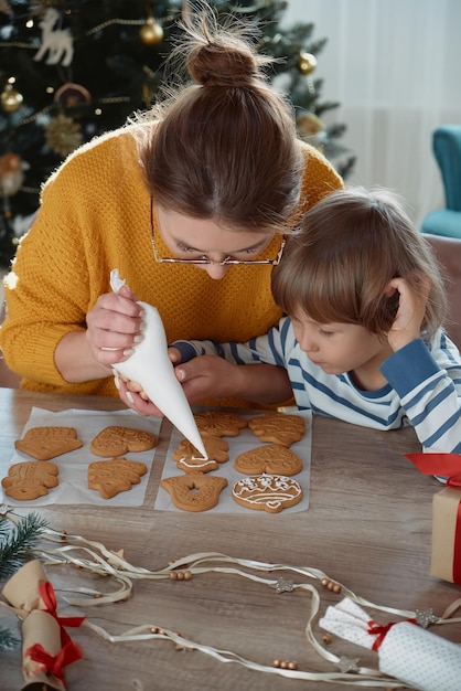 Mutter und Kind schmücken gemeinsam Weihnachtslebkuchen mit Puderzucker