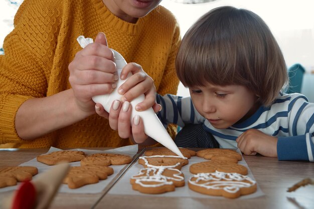 Mutter und Kind schmücken gemeinsam Weihnachtslebkuchen mit Puderzucker