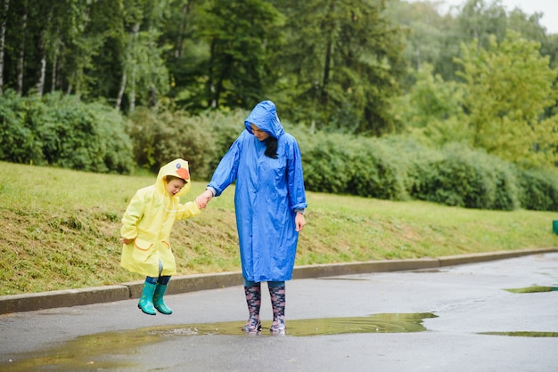 Mutter und Kind spielen im Regen, tragen Stiefel und Regenmäntel