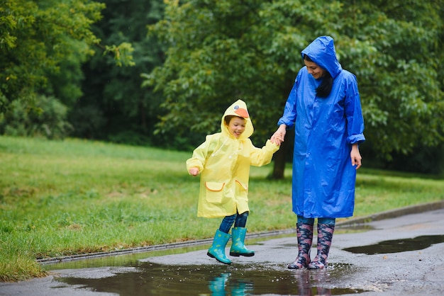 Mutter und Kind spielen im Regen, tragen Stiefel und Regenmäntel