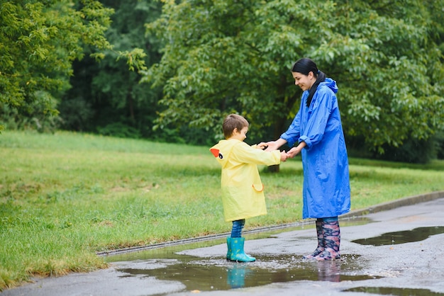 Mutter und Kind spielen im Regen, tragen Stiefel und Regenmäntel