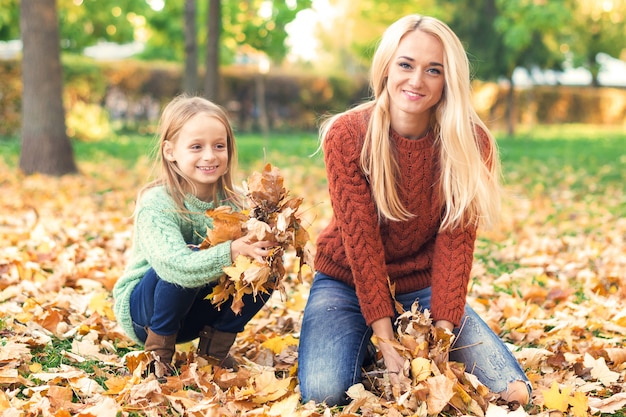 Mutter und Kind spielen mit Blättern im Herbst