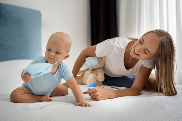 Mutter und Kind spielen mit Teddybär und medizinischer Maske