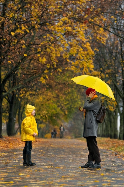 Mutter und Kind stehen im Herbstpark im Regen Gehen bei Regenwetter Vertikaler Rahmen