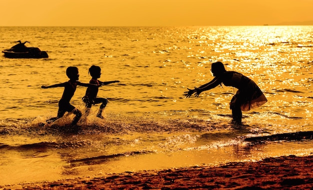 Mutter und Kinder, die am Strand zur Sonnenuntergangzeit spielen. Konzept der freundlichen Familie.