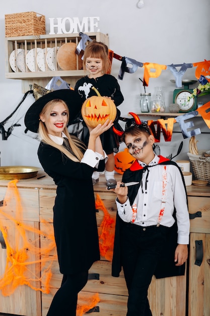 Mutter und Kinder in der Küche, die im Abendkleid steht und das cameraHalloween betrachtet