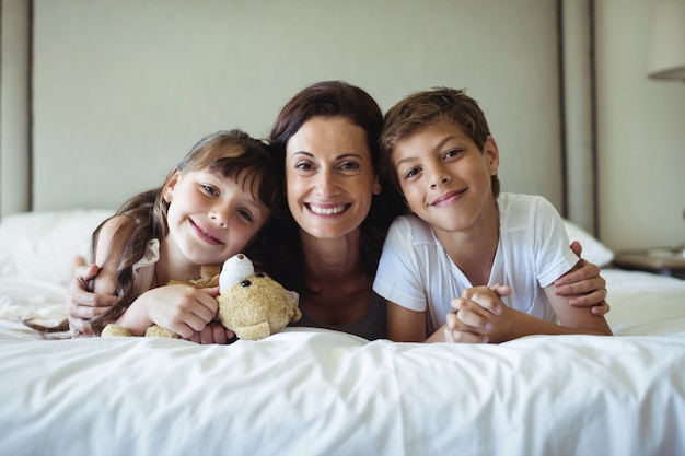 Mutter und Kinder liegen auf Bett mit Teddybär im Schlafzimmer