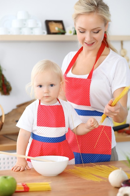 Mutter- und Kindertochter, die Teigwaren oder Salat für das Frühstück kocht. Konzept der glücklichen Familie in der Küche.