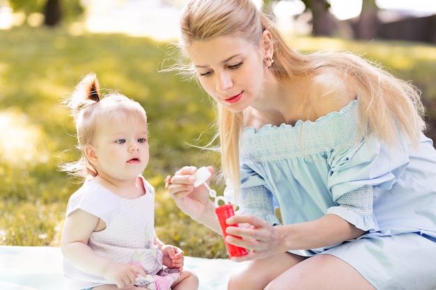 Mutter und kleine kleine Tochter, die Seifenblasen im Freien bläst