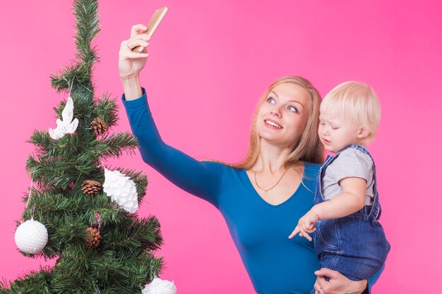 Mutter und kleine Tochter nehmen ein Selfie nahe Weihnachtsbaum