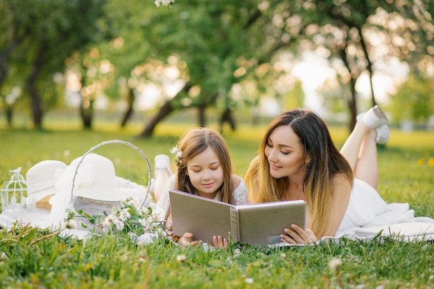 Mutter und kleine Tochter schauen sich im Sommer im Garten ein Familienalbum mit Fotos an. Familienwerte