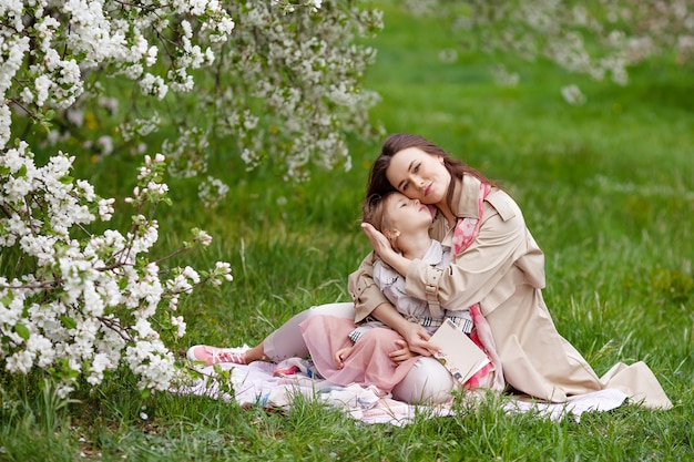 Mutter und kleine Tochter umarmen sich und gehen im blühenden Apfelgarten.