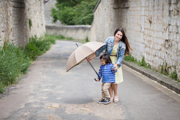 Mutter und kleiner östlicher hübscher Babyjunge spielen mit Regenschirm im Freien