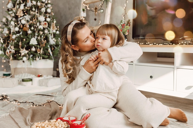 Mutter und kleines Kind haben Spaß und spielen zu Hause zusammen. Fröhliche Mutter umarmt süße kleine Tochter in der Nähe des Weihnachtsbaums. Frohe Weihnachten und schöne Feiertage.