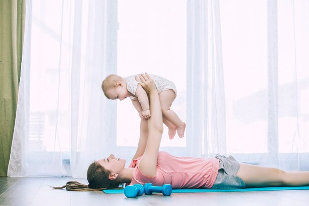 Mutter und kleines Kleinkind machen Fitness zu Hause auf einer Übungsmatte zusammen und lächeln zu Hause