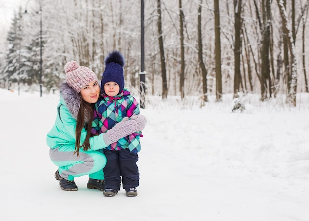 Mutter und kleines Kleinkindmädchen, das im Winterwald geht und Spaß mit Schnee hat. Familie