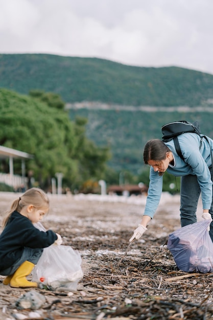 Mutter und kleines Mädchen sammeln Müll in Tüten am Strand