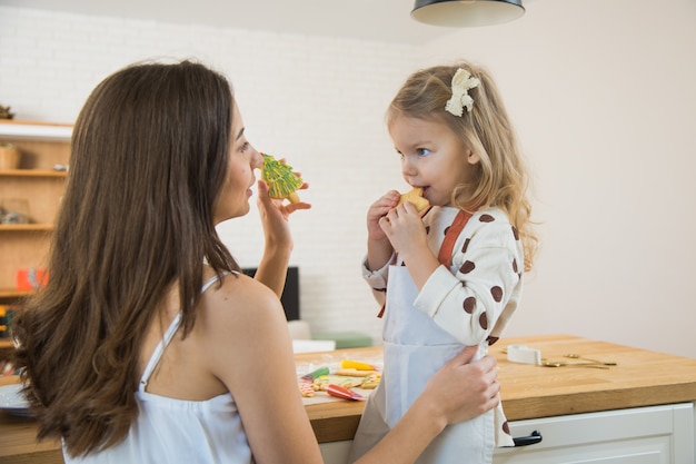 Mutter und Kleinkindtochter backen Lebkuchenplätzchen für Weihnachten. Dekorieren von hausgemachten Keksen für die Winterferien.