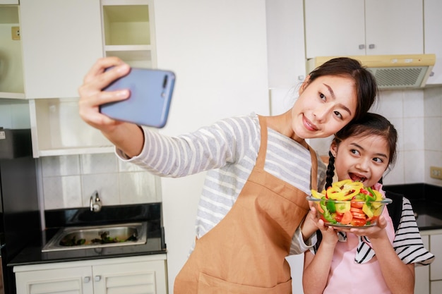 Mutter und Mädchen selfie per Smartphone beim Zubereiten von Salat in einer Küche zu Hause Freizeitaktivität