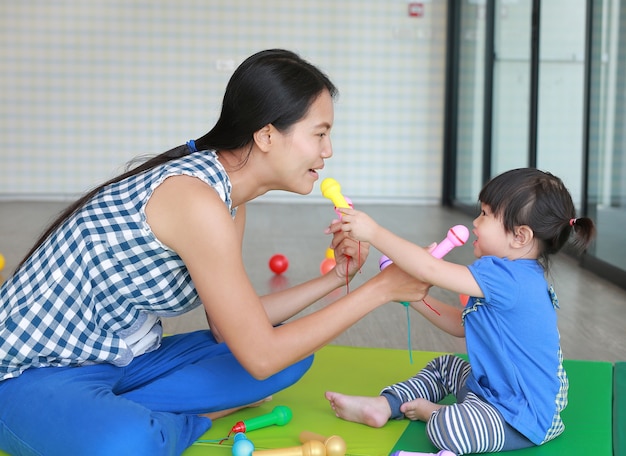 Mutter und nettes asiatisches Baby, die Plastikmikrofon am Kinderraum spielt