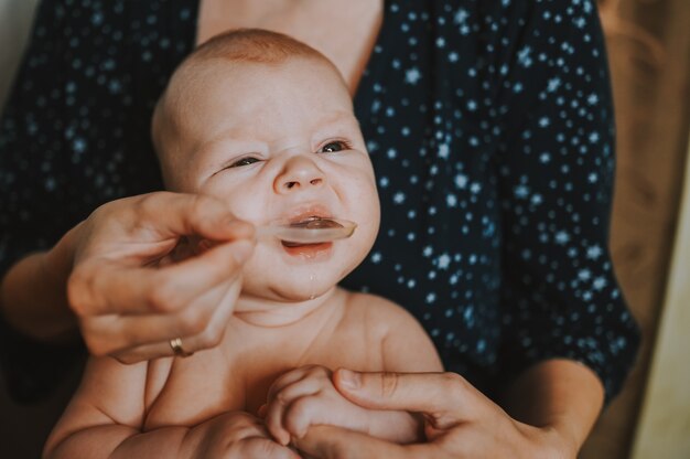 Mutter und Neugeborenes lustiges emotionales weinendes nacktes Baby des Säuglings nimmt flüssige Medikamente oder