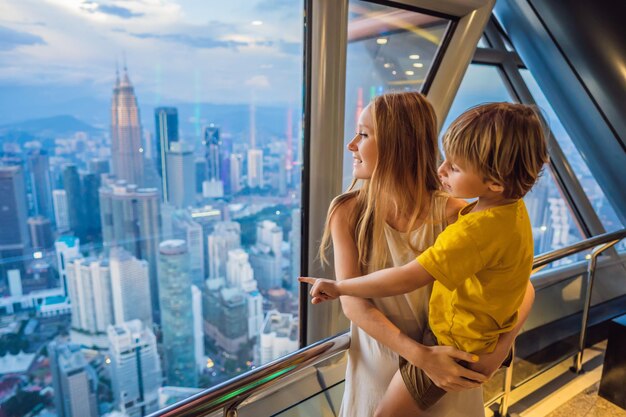 Mutter und Sohn betrachten das Stadtbild von Kuala Lumpur Panoramablick auf die Skyline der Stadt Kuala Lumpur Abend bei Sonnenuntergang Wolkenkratzer Gebäude in Malaysia Reisen mit Kindern Konzept