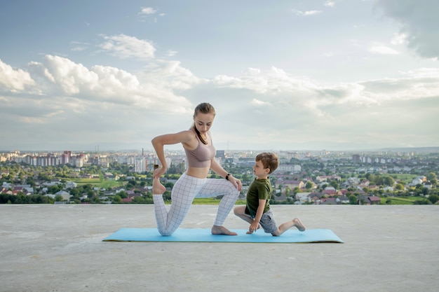 Mutter und Sohn, die Übung auf dem Balkon im Hintergrund einer Stadt während Sonnenaufgang oder Sonnenuntergang, Konzept eines gesunden Lebensstils tun.