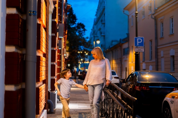 Mutter und Sohn, die in der Straße im Stadtzentrum spazieren gehen, Mutter und Kind, die einen Sommerabendspaziergang draußen machen?