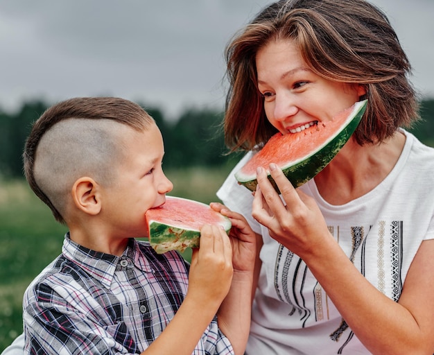 Mutter und Sohn essen Wassermelone auf der Wiese oder im Park Glückliche Familie auf Picknick im Freien Porträt Kleiner Junge und Mutter