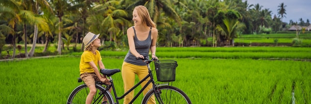 Mutter und sohn fahren fahrrad auf einem reisfeld in ubud bali reise nach bali mit kinderkonzeptbanner