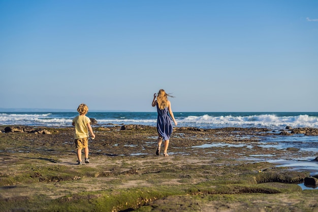 Mutter und Sohn gehen den kosmischen Strand von Bali entlang. Porträtreisetouristen - Mutter mit Kindern. Positive menschliche Emotionen, aktive Lebensstile. Glückliche junge Familie am Meeresstrand