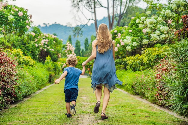 Mutter und Sohn laufen im blühenden Garten herum, glückliches Familienlebensstilkonzept