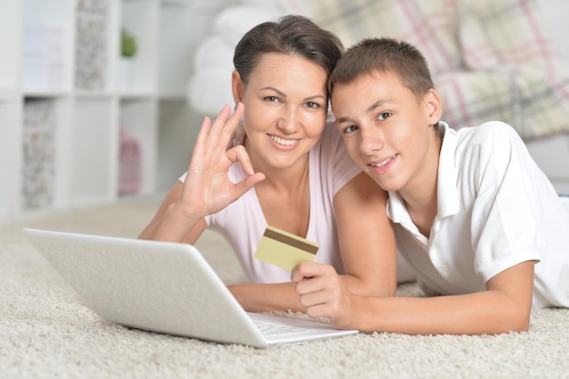 Mutter und Sohn liegen auf dem Boden und nutzen Laptop-Online-Shopping