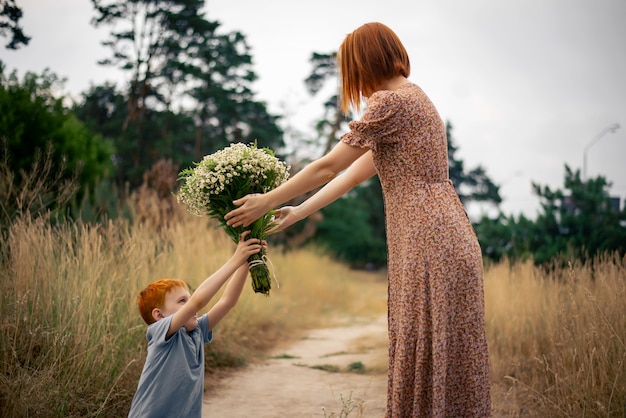 Mutter und Sohn mit roten Haaren mit einem großen Strauß Wildblumen in der Natur im Sommer