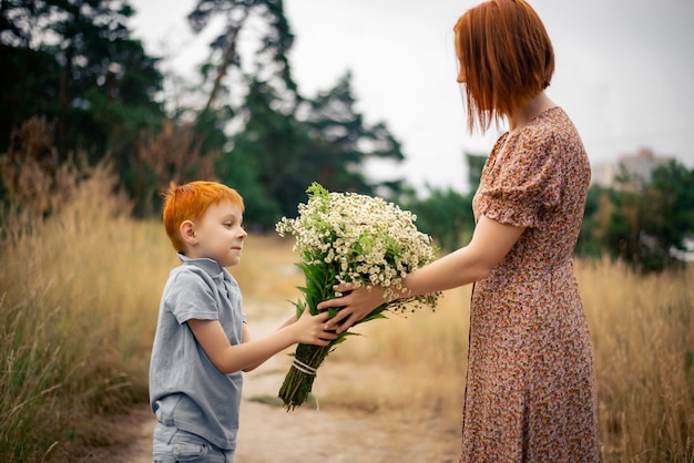 Mutter und Sohn mit roten Haaren mit einem großen Strauß Wildblumen in der Natur im Sommer