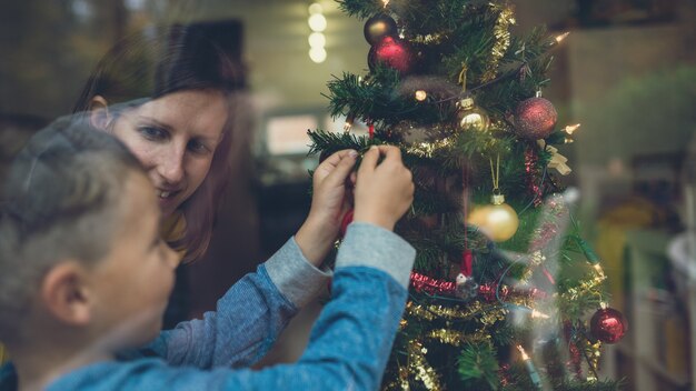 Mutter und Sohn schmücken zusammen den Weihnachtsbaum. Blick durch ein Fenster.