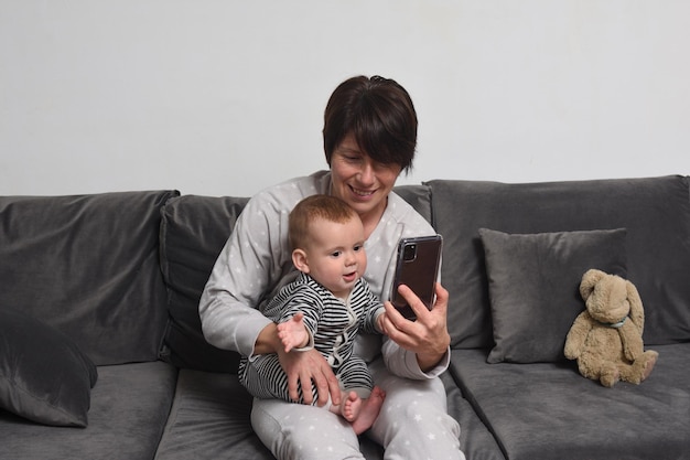 Mutter und Sohn sitzen auf dem Sofa, die Mutter zeigt dem Baby das Smartphone