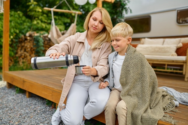 Mutter und Sohn trinken Tee aus einer Thermoskanne am Wohnwagen