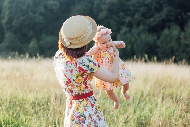 Mutter und süße kleine Tochter spielen auf dem Feld und kreisen mit Baby auf dem Feld. Eine Mutter geht mit einem Kind auf einem Sommerfeld spazieren.