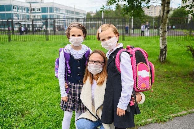 Mutter und süße Töchter mit Sicherheitsmaske. Schulmädchen bereit zur Schule.