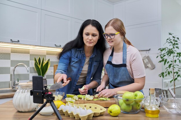 Foto mutter und teenie-tochter kochen zusammen apfelkuchen und schauen auf den smartphone-bildschirm