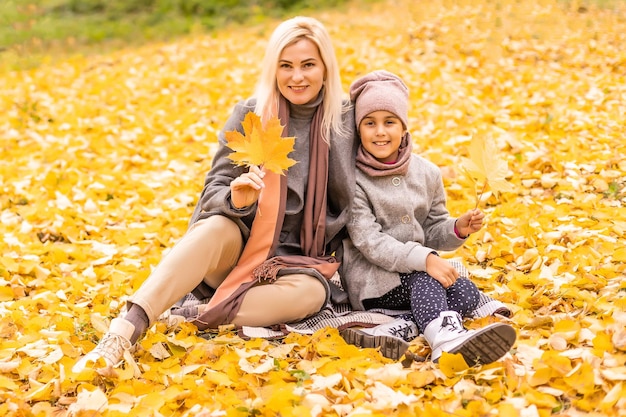 Mutter und Tochter amüsieren sich im Herbstpark zwischen den fallenden Blättern.