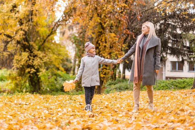 Mutter und Tochter amüsieren sich im Herbstpark zwischen den fallenden Blättern.