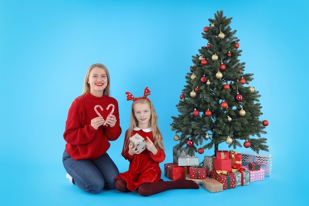 Mutter und Tochter auf blauem Hintergrund mit Weihnachtsbaum und Geschenken