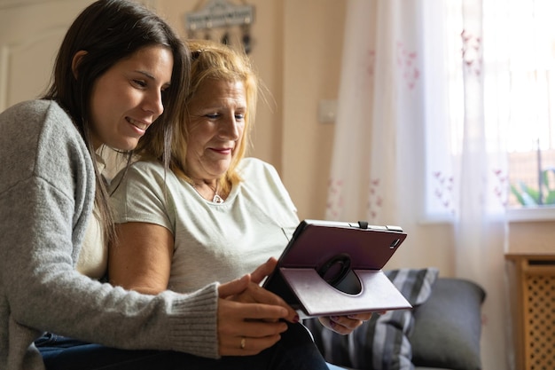 Mutter und Tochter auf dem Sofa zu Hause, während sie auf das Tablet schauen und glücklich sind