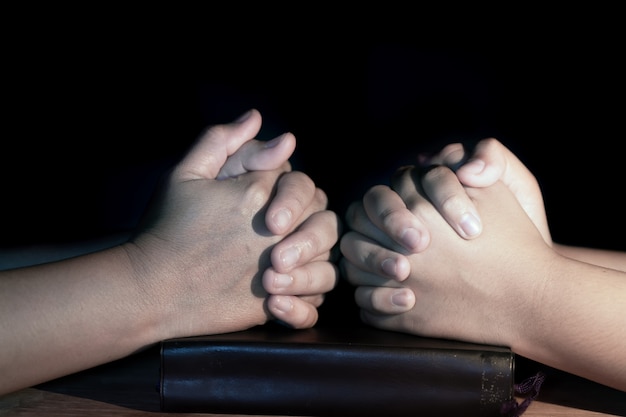 Mutter und Tochter beten zusammen über heilige Bibel auf Holztisch mit dem Licht fr