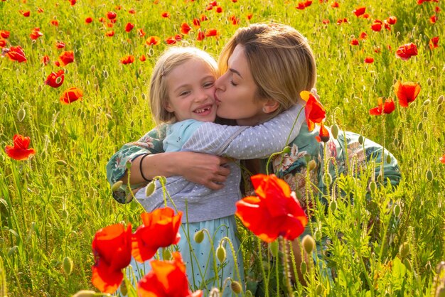 Mutter und Tochter, die auf blühendem Mohnfeld umarmt Sommerurlaub mit der Familie in der Natur Sommer auf der Mohnwiese mit Mohnblumen